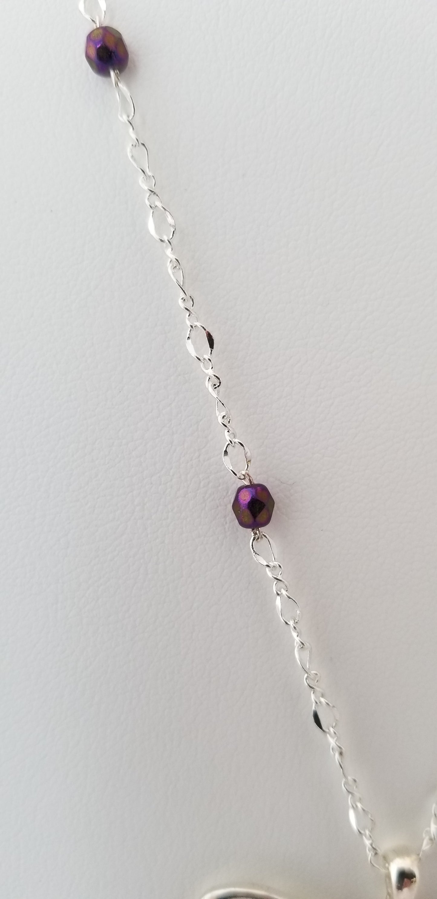 A silver necklace with a purple bead in the center.