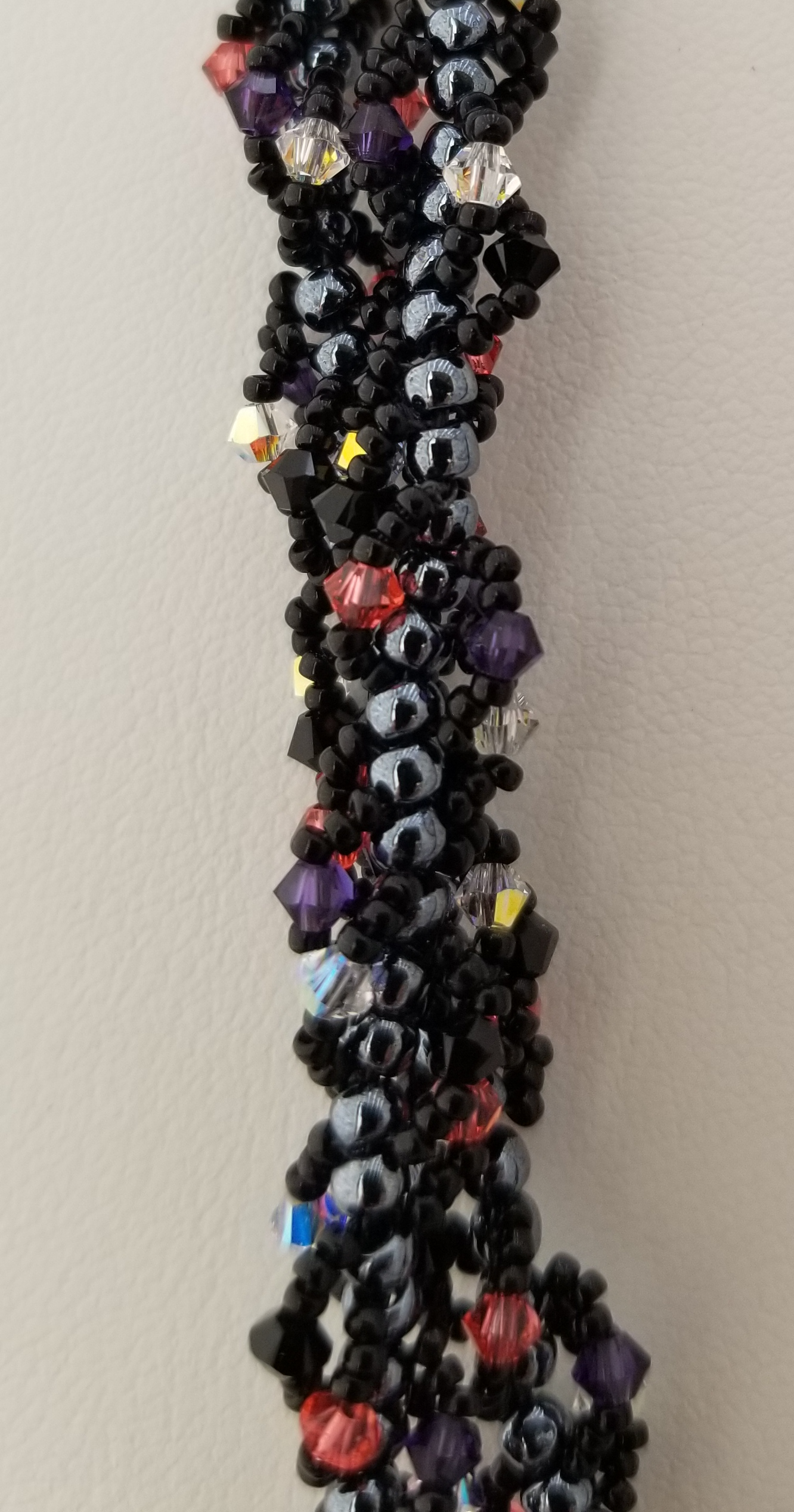 A close-up view of a colorful beaded necklace or bracelet, with a variety of beads in different colors and shapes, including black, purple, and red beads.