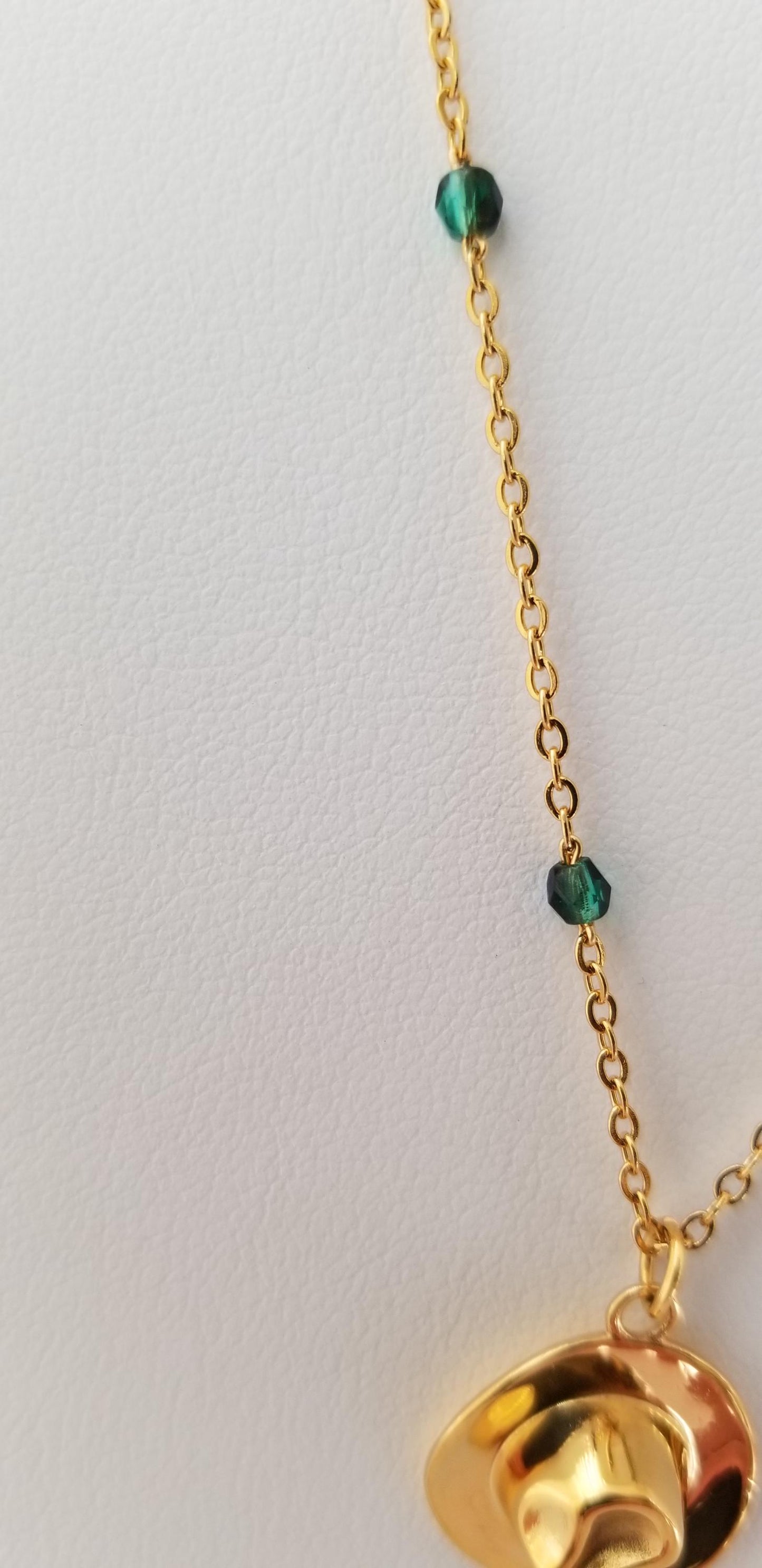 A gold necklace with a pendant and green gemstones is shown against a white background.