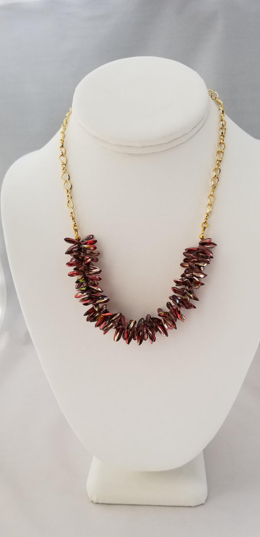 A necklace with a gold chain and a row of red and gold beads on a white mannequin head.