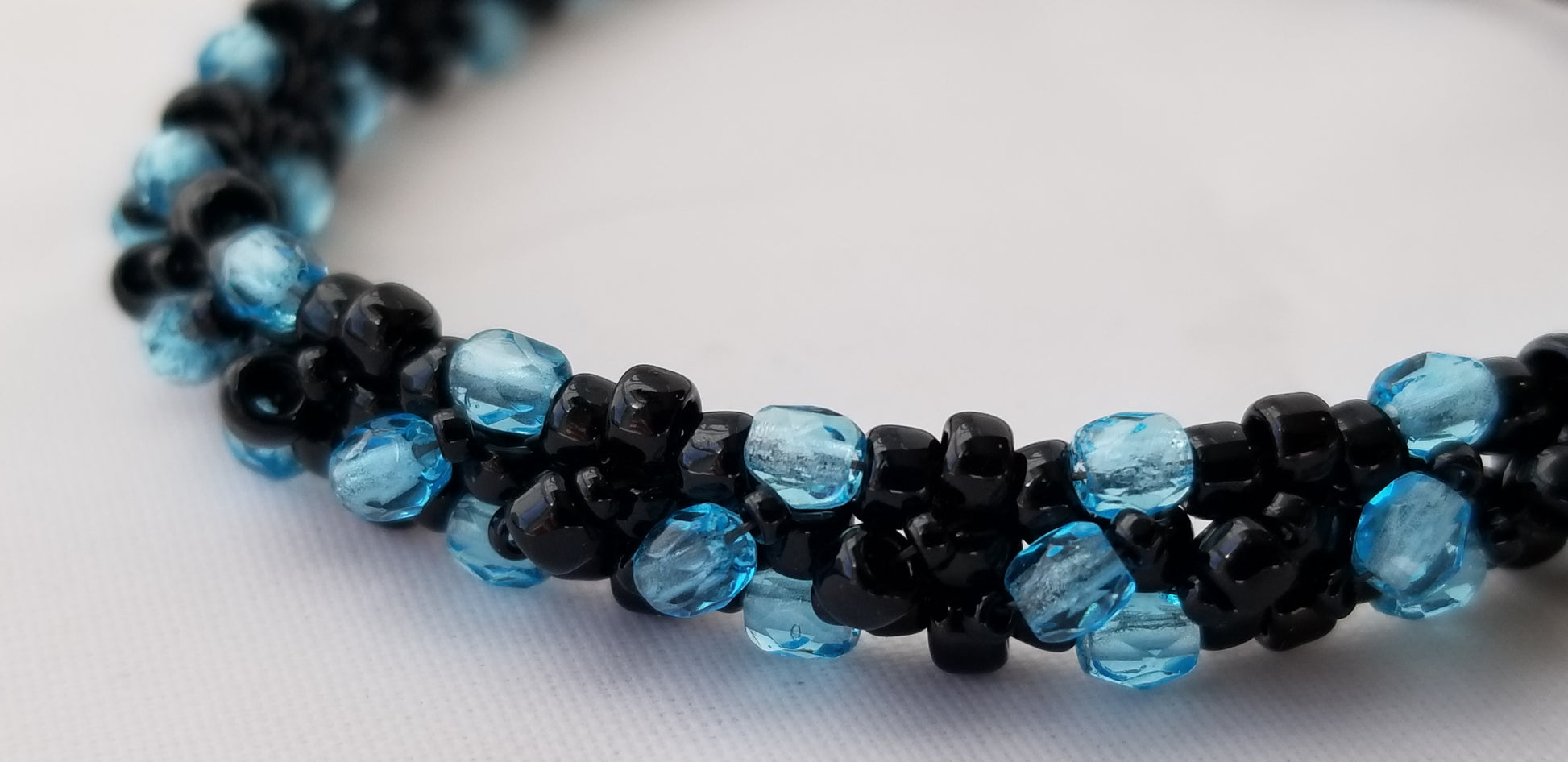 a blue and black beaded necklace on a white surface