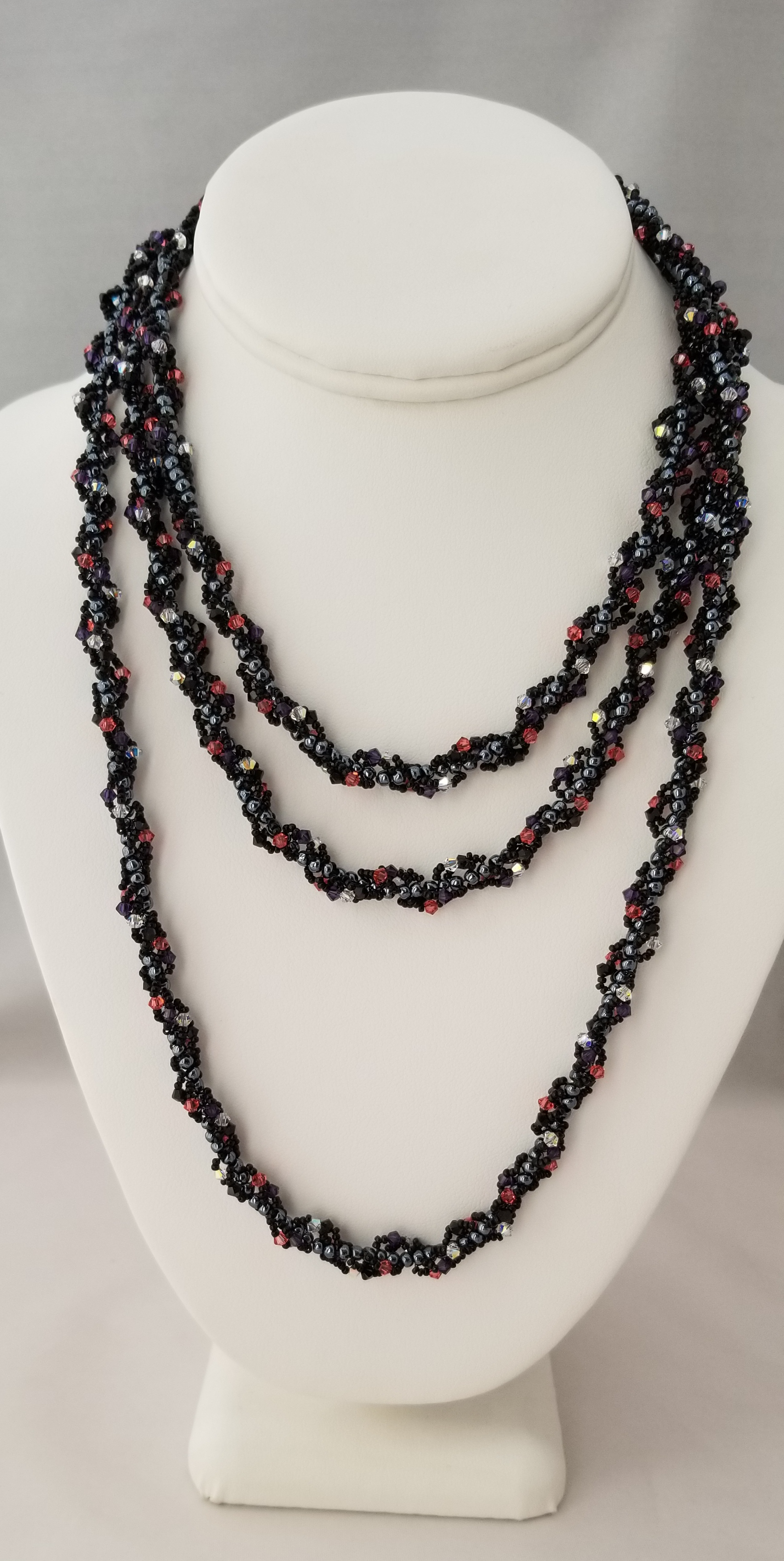A white bust form displaying a long, black beaded necklace with red and black beads.