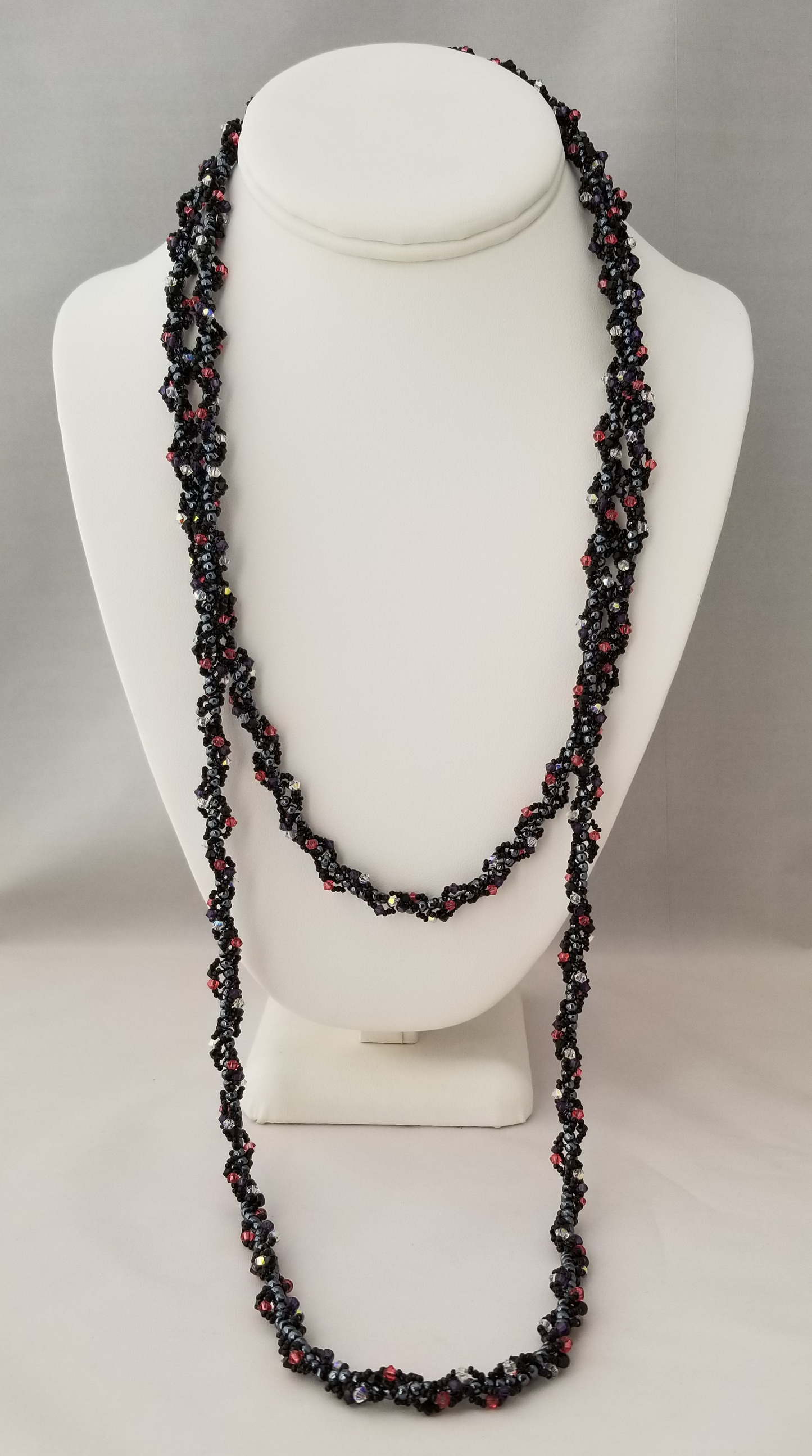 A long, black and red beaded necklace is displayed on a white bust form against a gray background.