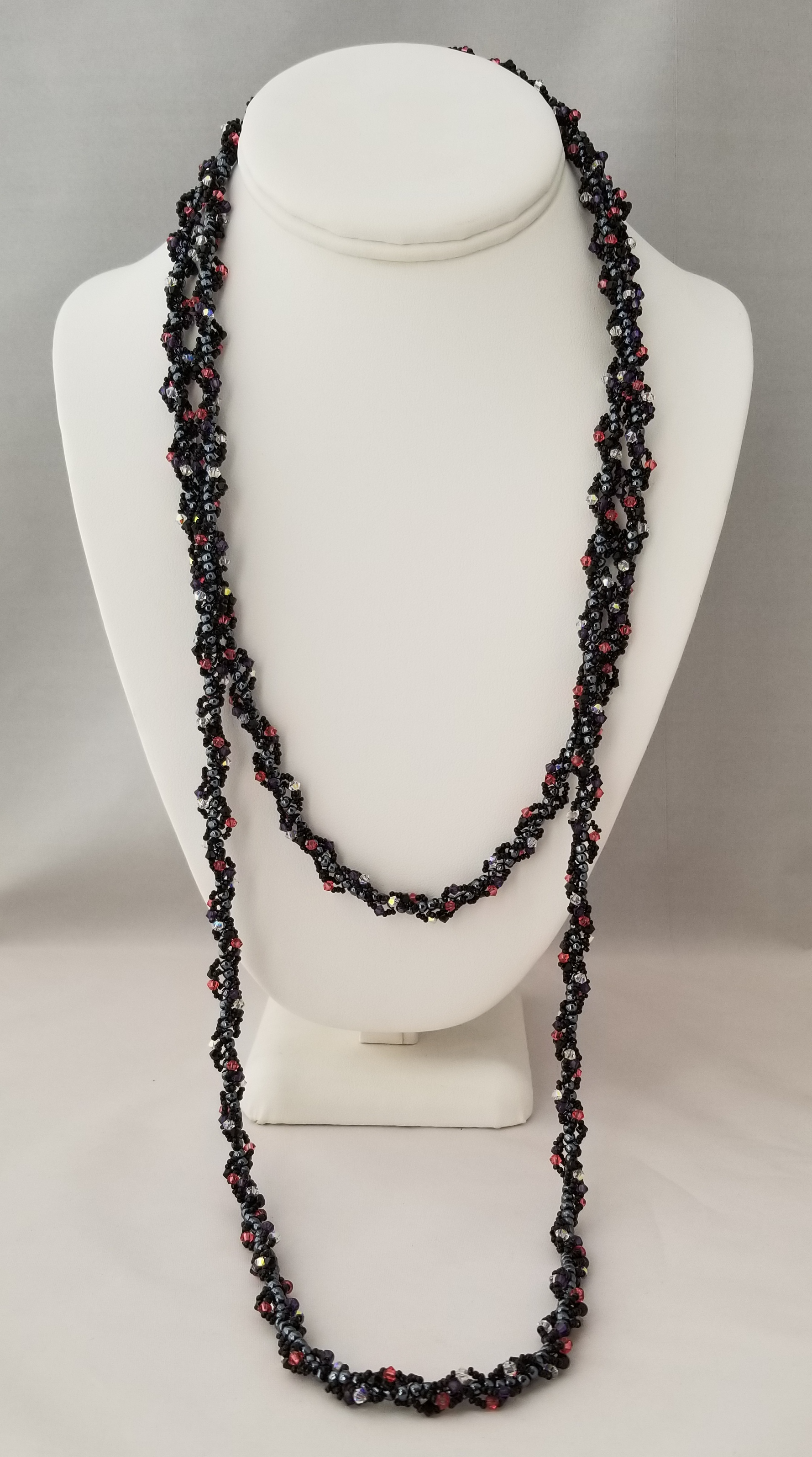 A long, black and red beaded necklace is displayed on a white bust form against a gray background.
