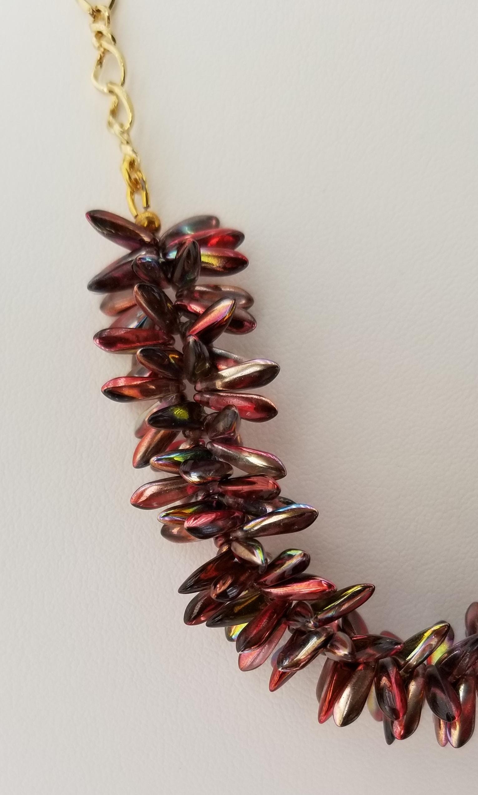 A close-up view of a necklace with a long chain made of small, shiny beads in a burgundy or red color.