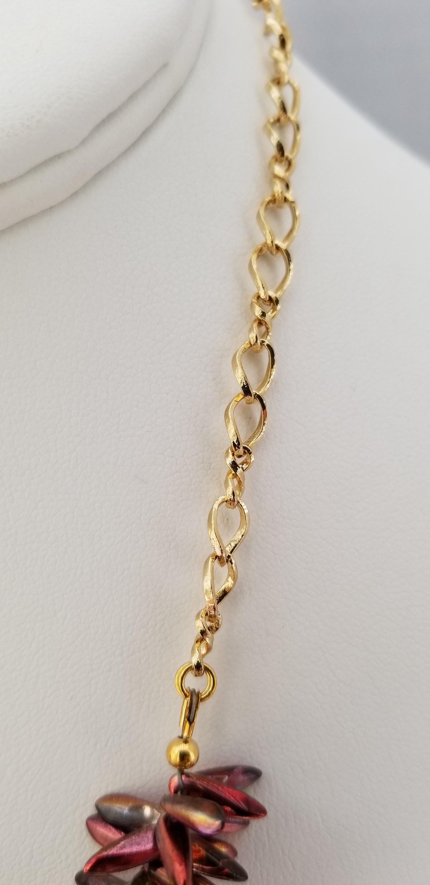 A close-up view of a gold chain necklace with a pendant featuring red and purple gemstones.