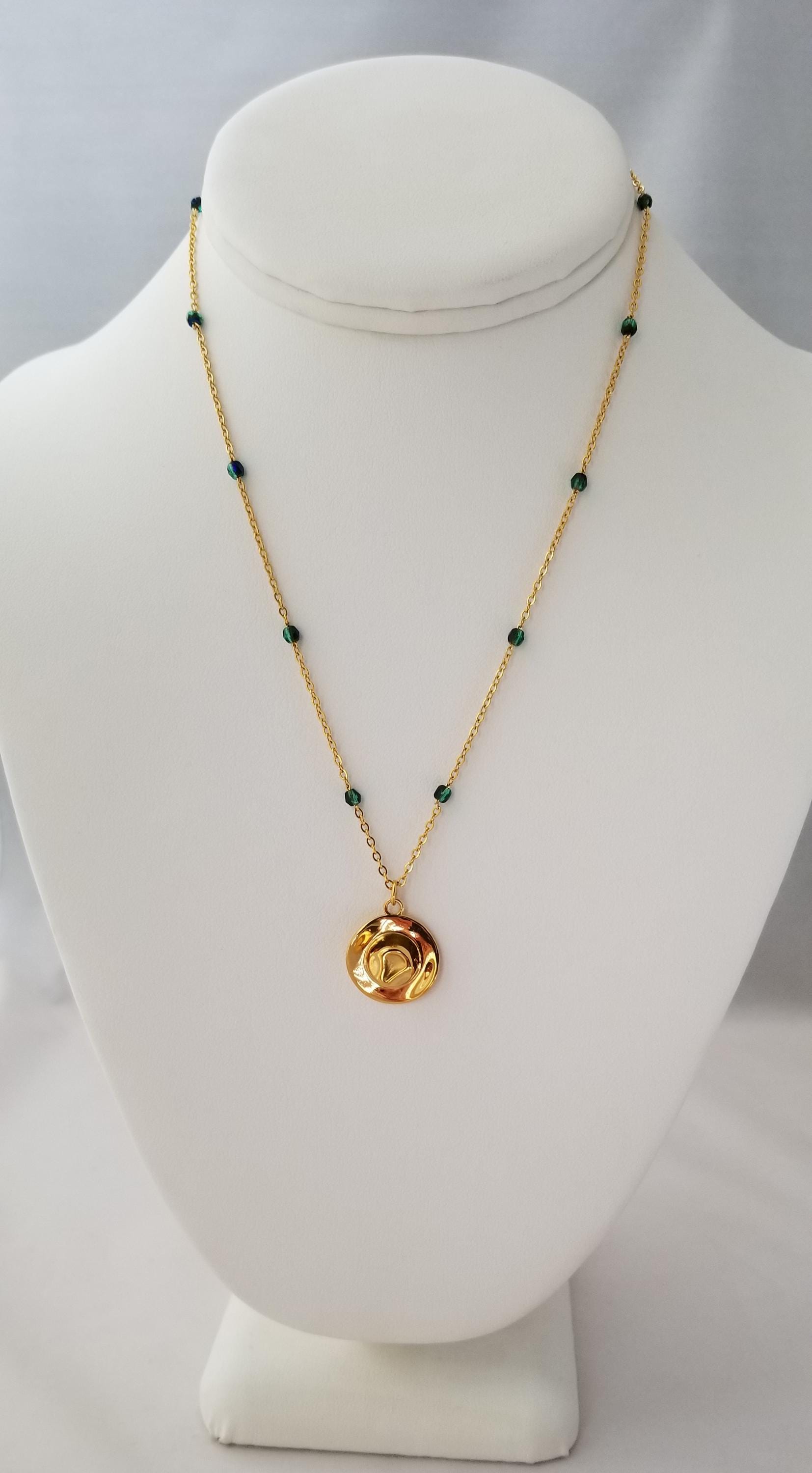 A gold necklace with green beads and a round pendant is displayed on a white bust form.