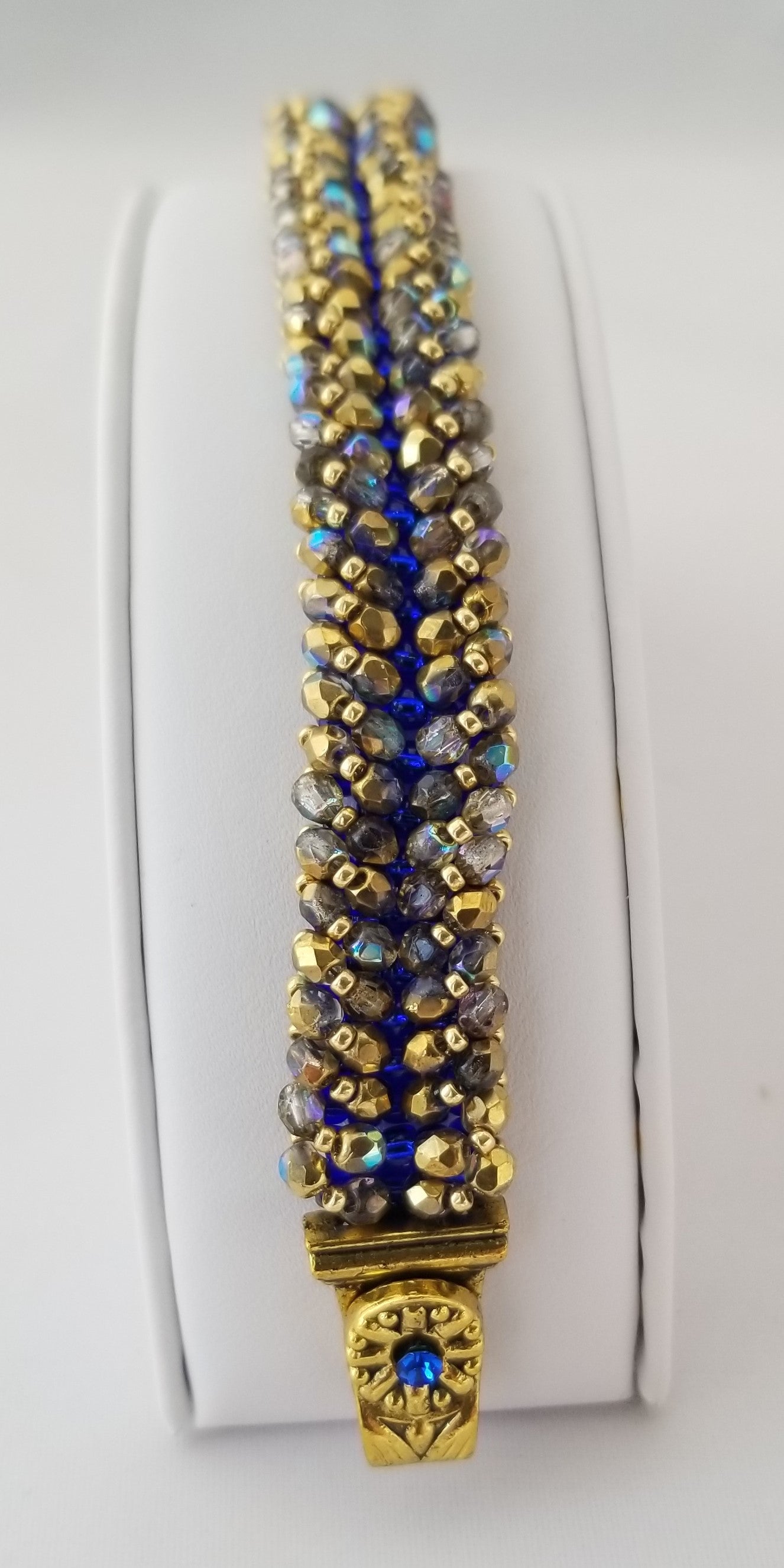 a gold and blue beaded bracelet on a white surface