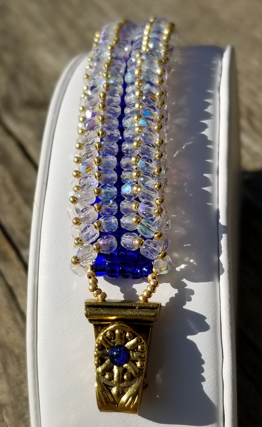 a gold and blue beaded necklace on a white box
