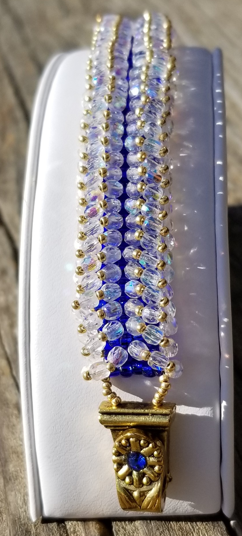 a gold and blue beaded necklace on a white box